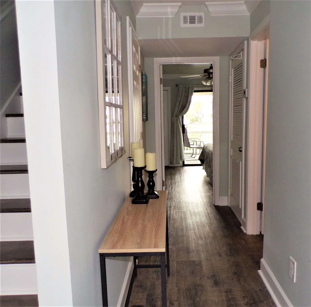A welcoming hallway leads toward a bedroom with a balcony and outdoor seating, offering a glimpse of the lake beyond. The console table with candles and a decorative mirror adds warmth, while the view hints at the easy transition from indoor comfort to lakeside relaxation.